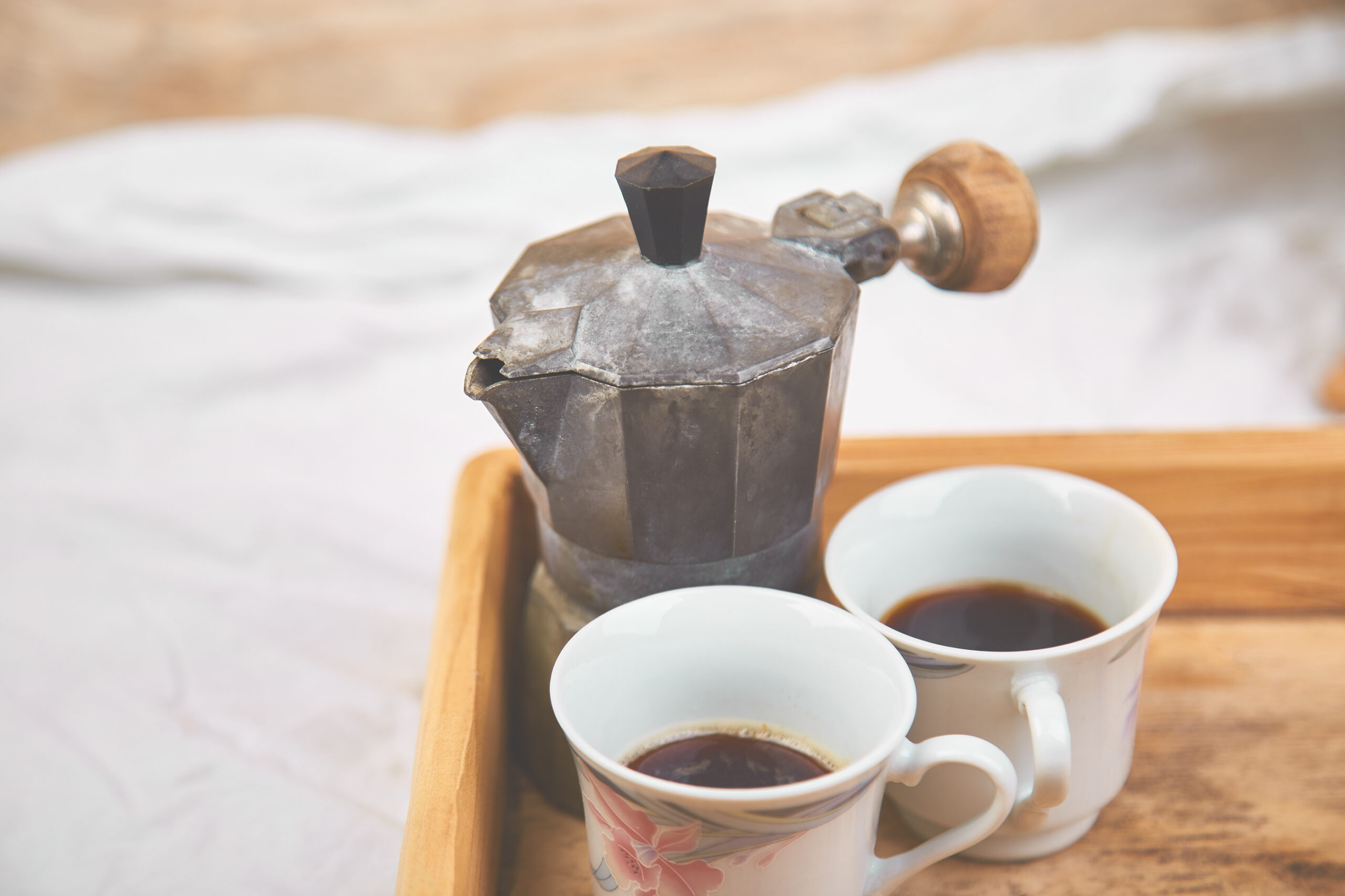 Moka coffee pot with two cup of coffe on wooden tray on white background. Old style italian coffee in soft vintage tone. Copy space.