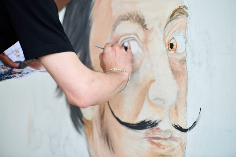 Young man artist draws with paint brush surreal man portrait on white canvas art painting festival